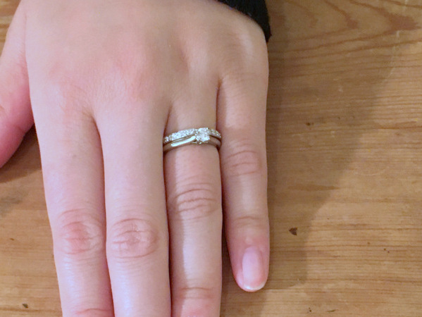 女性の手にプラチナダイヤモンドの婚約指輪とリボンのようなデザインの結婚指輪