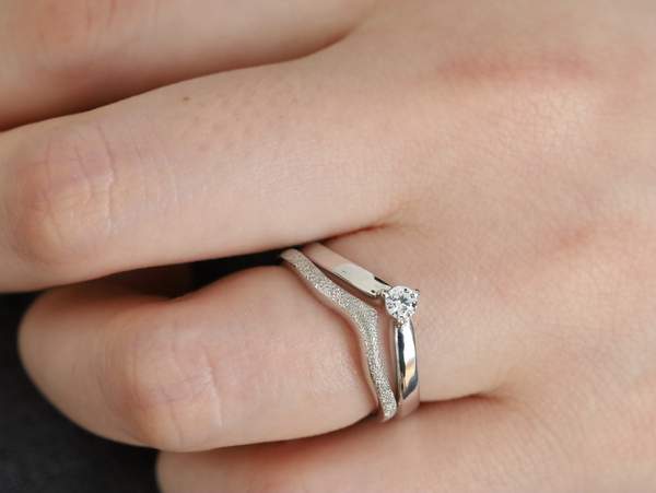 V字の結婚指輪と婚約指輪を重ねづけした女性の手