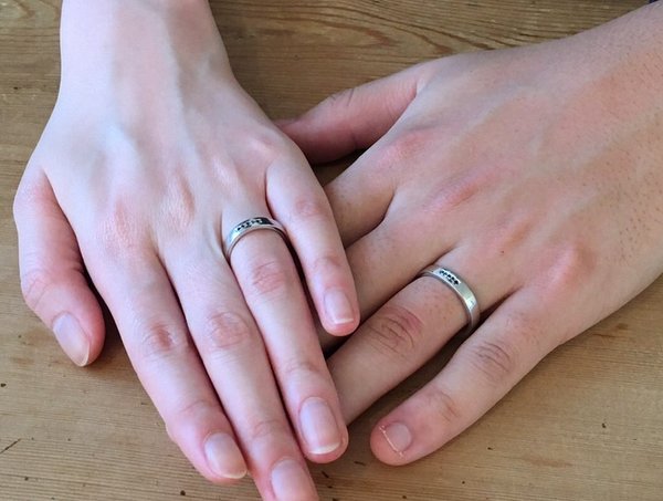 平打ちにブラックダイヤモンドが石留されたプラチナの結婚指輪をするカップルの手